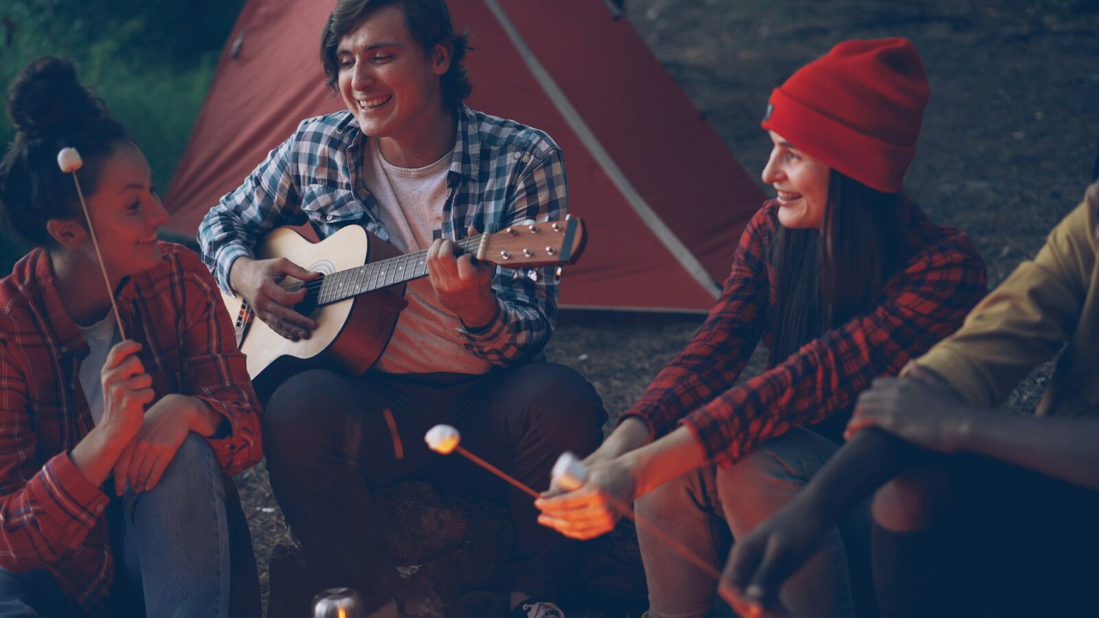Des amis réunis autour d'un feu de camp le soir, l'un d'eux joue de la guitare